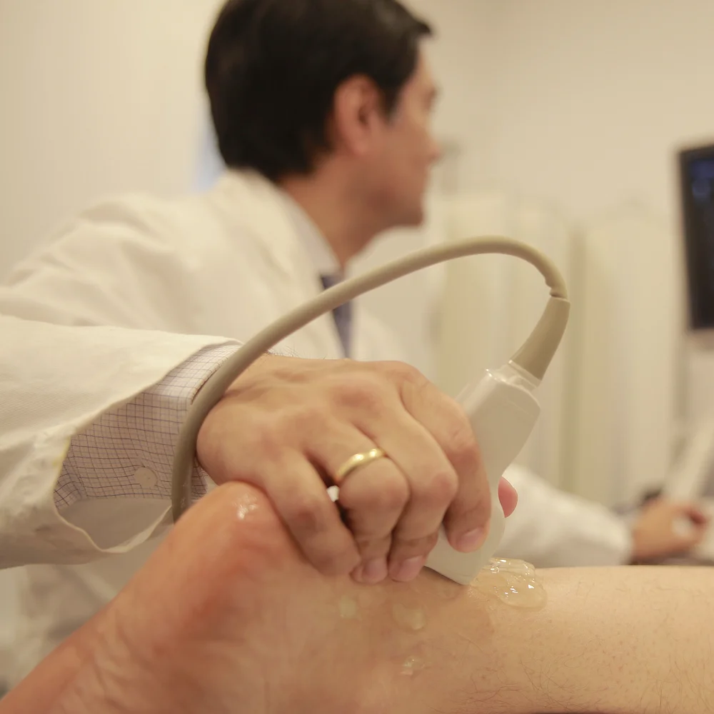Orthopaedic specialist performing an ultrasound examination on a patient’s ankle to assess joint and soft tissue condition in a medical consultation room.