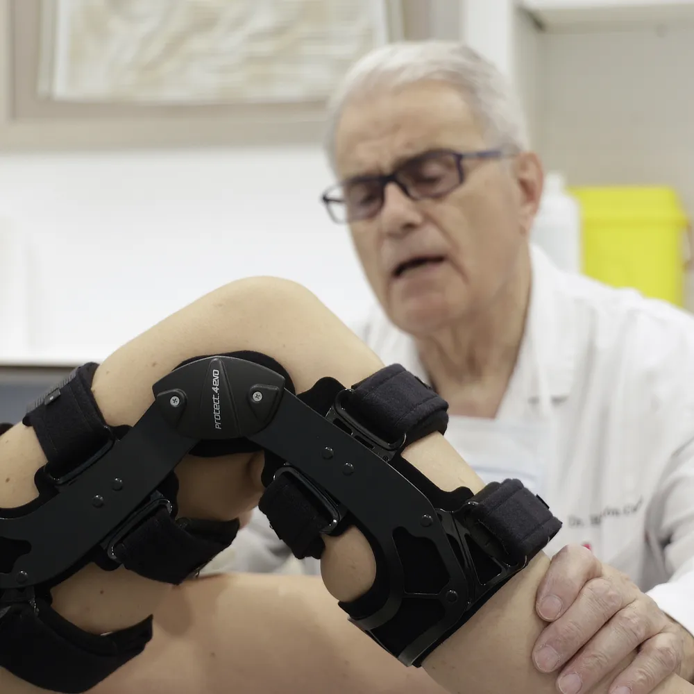Doctor Ramon Cugat examining a patient’s knee fitted with a black brace to evaluate stability and recovery progress after a sports injury or ligament surgery.