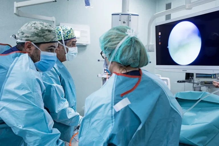 Surgical team in blue gowns performing an arthroscopic procedure, with a monitor displaying the joint interior, at Instituto Cugat’s Surgery Unit.